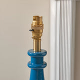Close-up of the Endon Carlworth table lamp's marlin blue resin spindle base and switched brass B22 lamp holder, shown beside a white curtain.