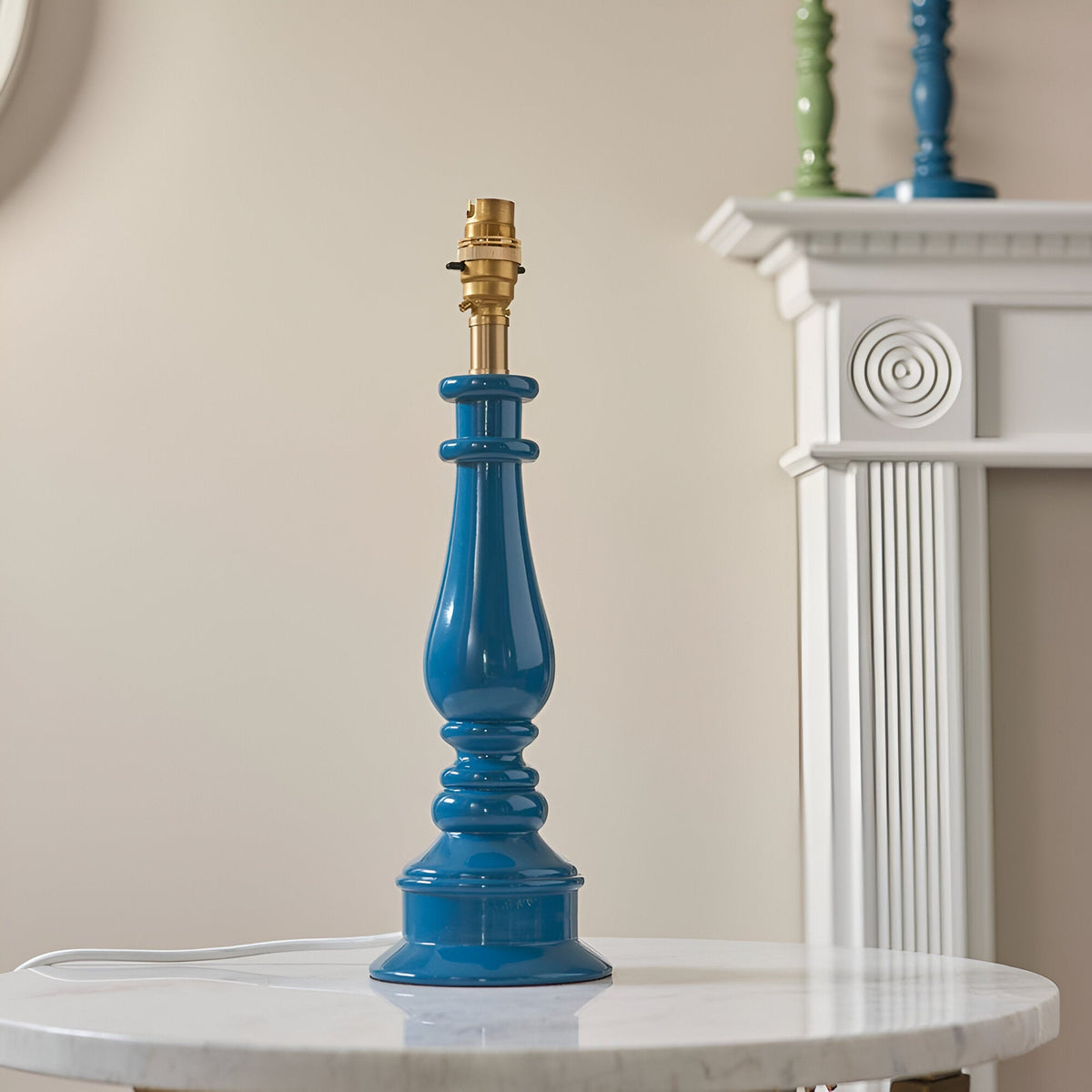 Endon Carlworth Ivy table lamp base in glossy blue turned resin with brass B22 lamp holder, displayed on a marble side table beside a white mantelpiece.