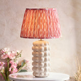 Amberley Ikat table lamp with a bobble-textured white ceramic base and pleated pink, orange and grey Ikat-print shade on a marble table.