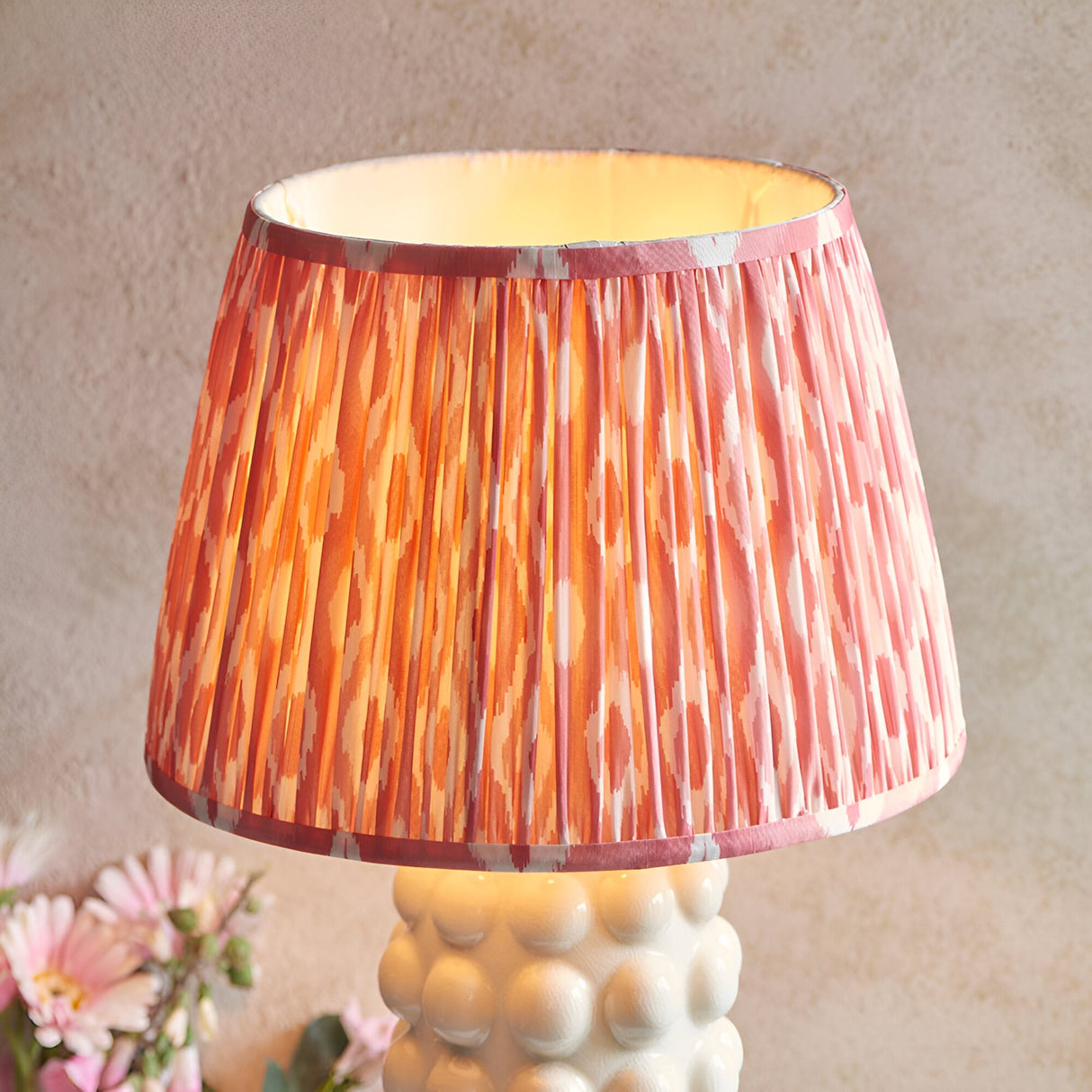 Amberley Ikat table lamp with pleated pink, orange and white ikat fabric shade on a white sculptural bobble ceramic base, shown against a neutral background.
