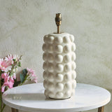 Amberley Ikat Table Lamp base with sculptured white ceramic bobble body and brass fitting, shown on a marble side table beside pink flowers.
