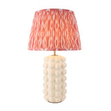 Amberley Ikat table lamp with a white ceramic bobble base and a pleated pink and white patterned Ikat shade, brass stem detail, on a plain white background.