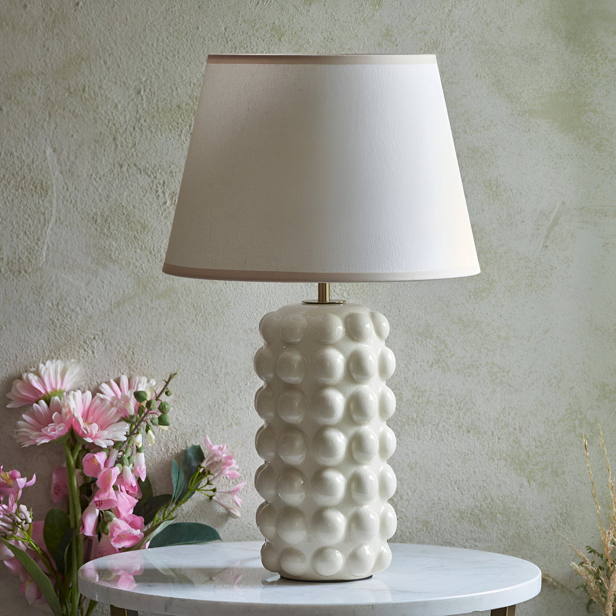 Endon Amberley Ivy table lamp with vintage white crackle-glazed ceramic bobble base and tapered white shade, on a marble table beside pink flowers.