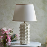 Endon Amberley Ivy table lamp with vintage white crackle-glazed ceramic bobble base and tapered white shade, on a marble table beside pink flowers.