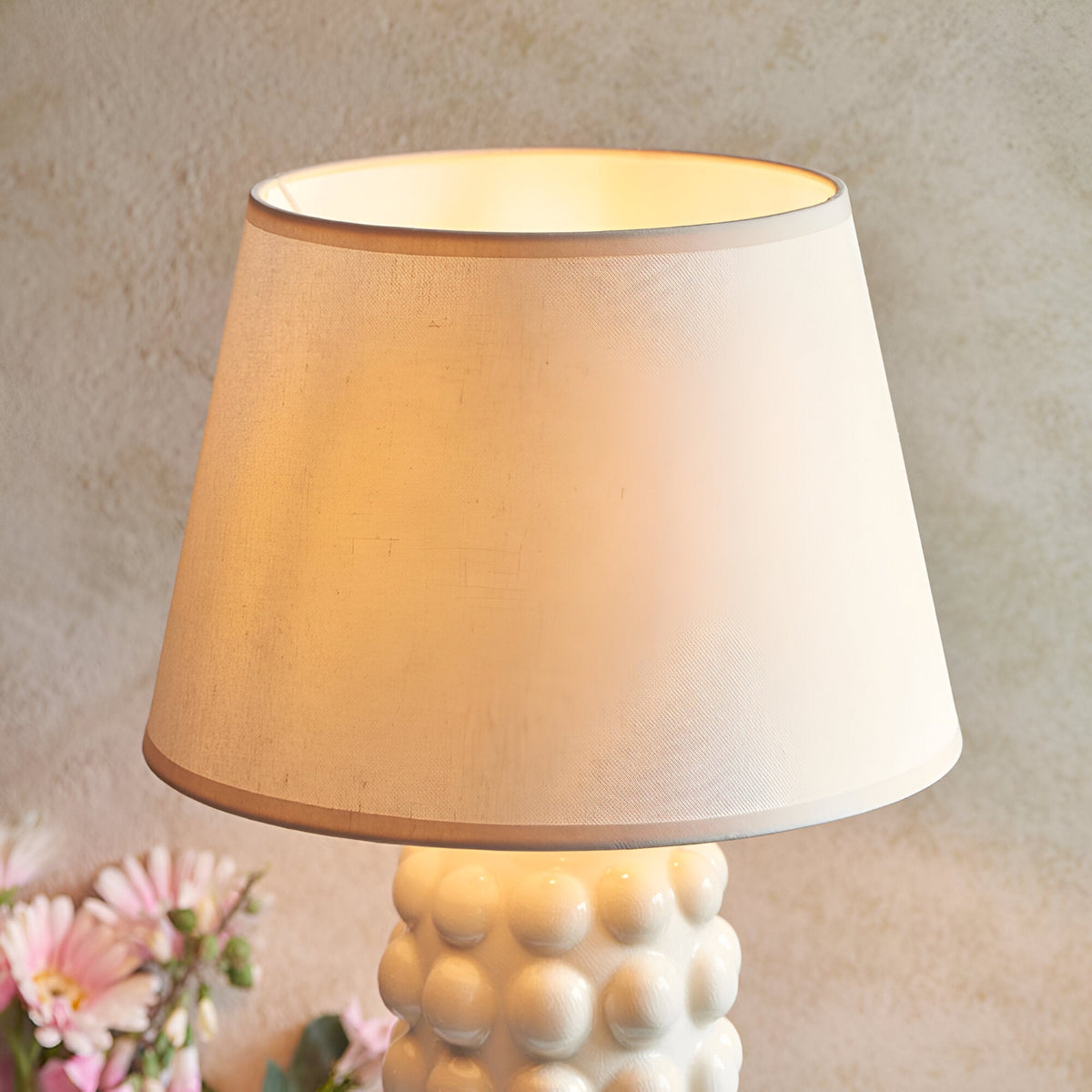 Endon Amberley Ivy table lamp close-up showing the illuminated tapered white cotton-mix shade above the vintage white crackle-glazed ceramic bobble base.