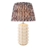 Amberley Ikat table lamp with a bobble-textured cream ceramic base, brass stem, and pleated grey-brown ikat print shade on a white background.