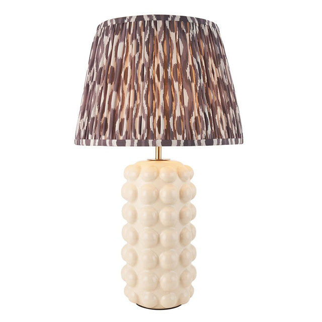 Amberley Ikat table lamp with a bobble-textured cream ceramic base, brass stem, and pleated grey-brown ikat print shade on a white background.