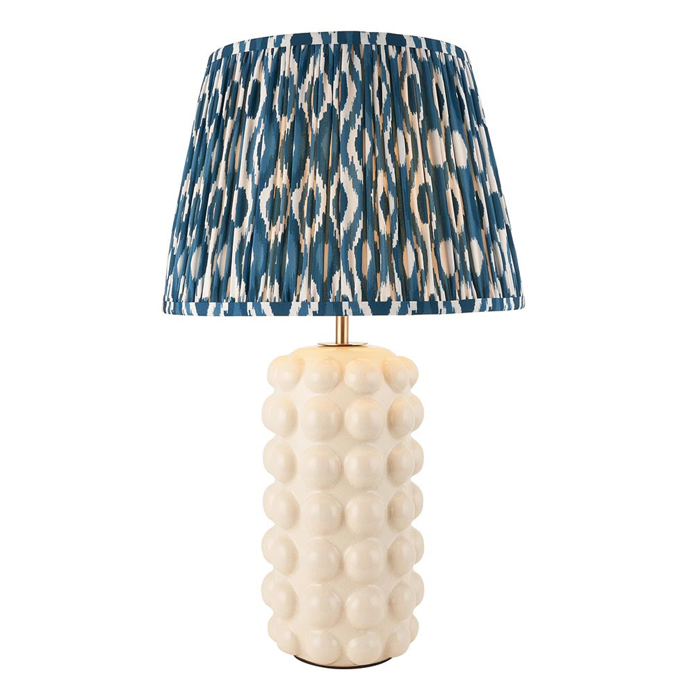 Endon Amberley Ikat table lamp with white ceramic bobble base, brass stem and pleated blue and white Ikat shade on a plain background.