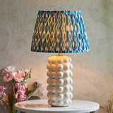 Endon Amberley Ikat table lamp with white ceramic bobble base, brass stem and pleated blue, grey and white ikat shade on a marble table.