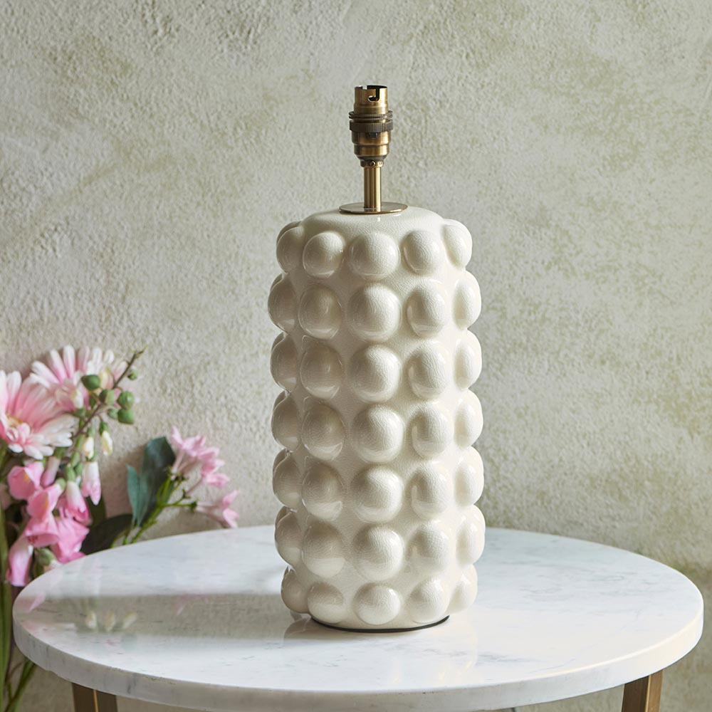 Endon Amberley Ikat table lamp base in white crackle-glazed ceramic with bobble texture, aged brass B22 holder, on a marble table beside pink flowers.
