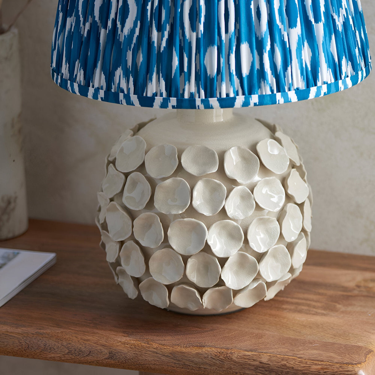 Ashbury Ikat Table Lamp in Blue, close-up of ceramic base with textured ivory crackle-glaze petals under a pleated blue and white patterned shade.