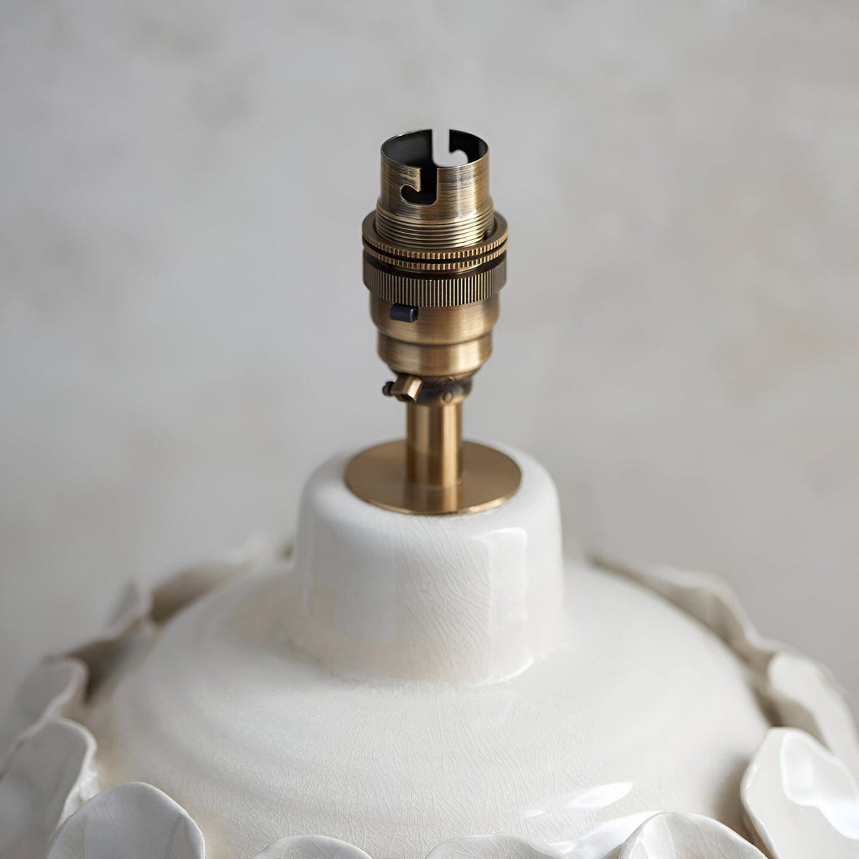 Close-up of the Ashbury table lamp's antique brass switched B22 lamp holder atop an ivory crackle-glaze ceramic base with fluted white shade edge.