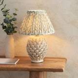 Endon Caldford table lamp with ivory crackle-glazed ceramic artichoke base and pleated green leaf-print shade on a wooden console beside a eucalyptus vase.