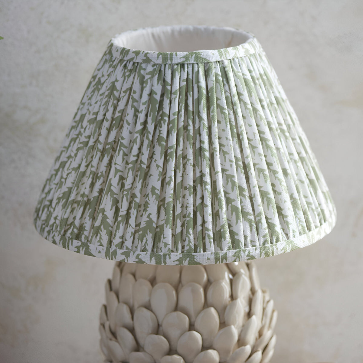Endon Caldford table lamp with pleated green and white leaf-print fabric shade above an ivory crackle-glazed ceramic base with layered leaf details.