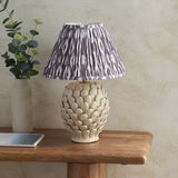 Endon Caldford table lamp with ivory ceramic leaf-textured base and pleated grey Ikat shade, styled on a wood console with a eucalyptus vase.
