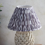 Endon Caldford table lamp with pleated grey and white Ikat fabric shade above an ivory crackle-glaze ceramic base with sculpted leaf detailing.