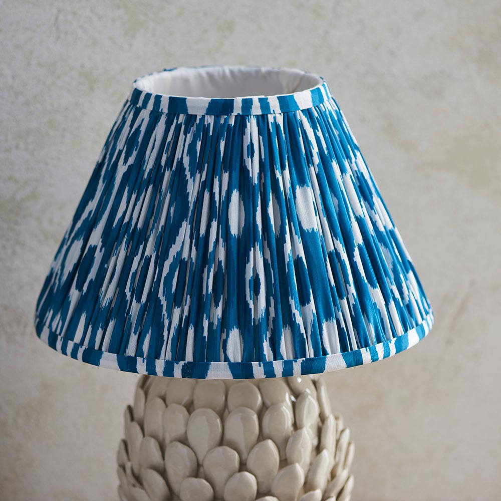 Caldford Ikat 30cm Table Lamp with pleated blue and white patterned fabric shade on a cream ceramic leaf-textured base, shown against a neutral background.