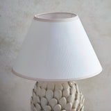 Caldford Ivy 30cm table lamp with white cotton-mix empire shade and almond trim, shown atop a leaf-textured ceramic base against a neutral background.