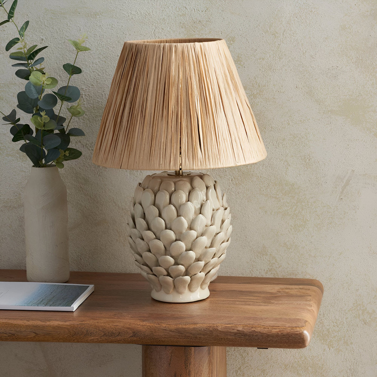 Endon Caldford ceramic table lamp with ivory crackle-glazed leaf-textured base and tapered natural raffia shade, styled on a wood console with eucalyptus.