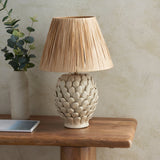 Endon Caldford ceramic table lamp with ivory crackle-glazed leaf-textured base and tapered natural raffia shade, styled on a wood console with eucalyptus.