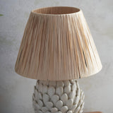 Endon Caldford table lamp close-up showing the tapered natural raffia shade above an ivory crackle-glazed ceramic base with leaf-shaped detailing.