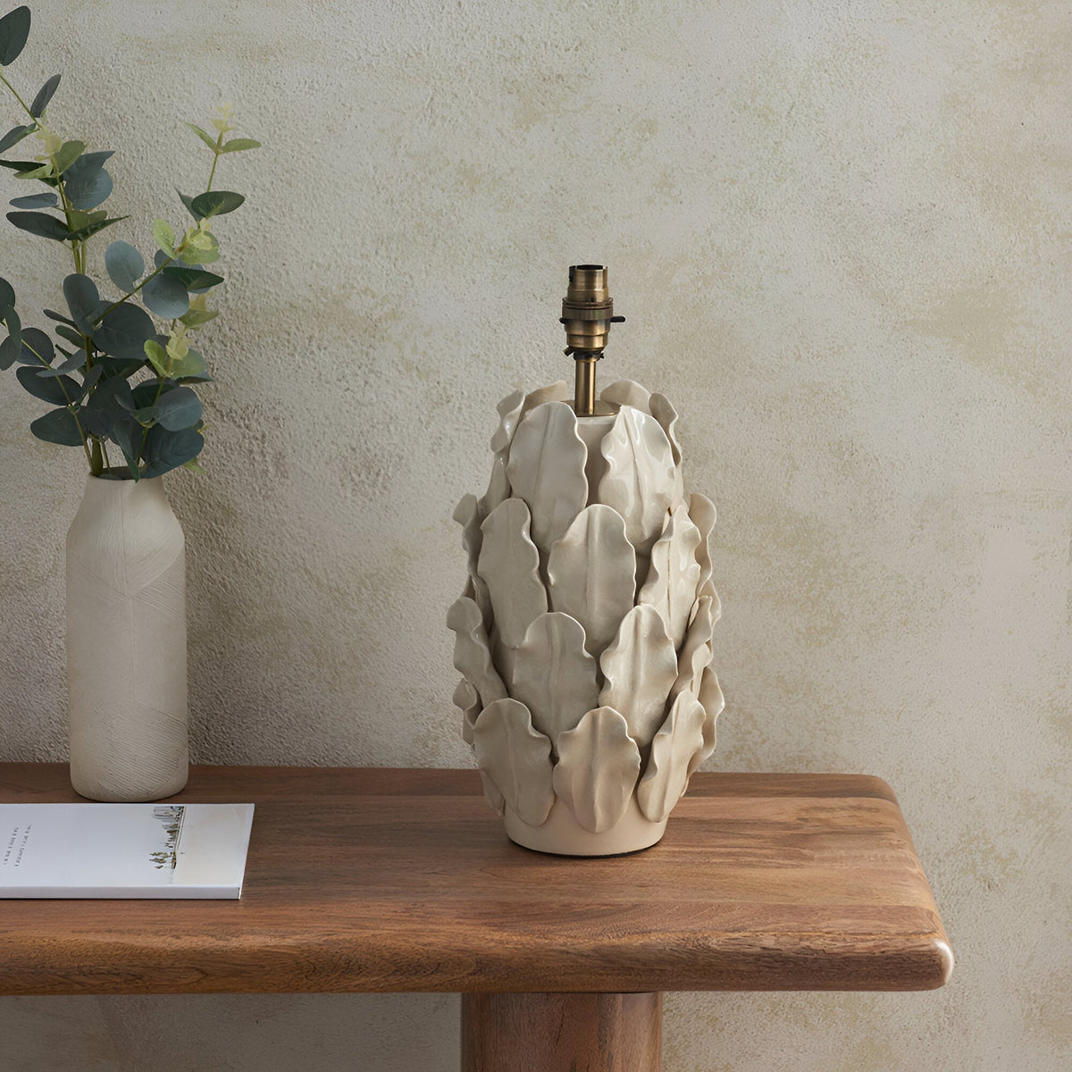 Caldford Ivy 35cm Table Lamp base in ivory ceramic with layered leaf detailing and brass B22 holder, shown on a wooden console table beside a vase.