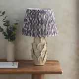 Endon Caldford Ikat 35cm table lamp with ivory crackle-glaze ceramic leaf base and grey pleated Ikat shade, on a wooden console with eucalyptus.