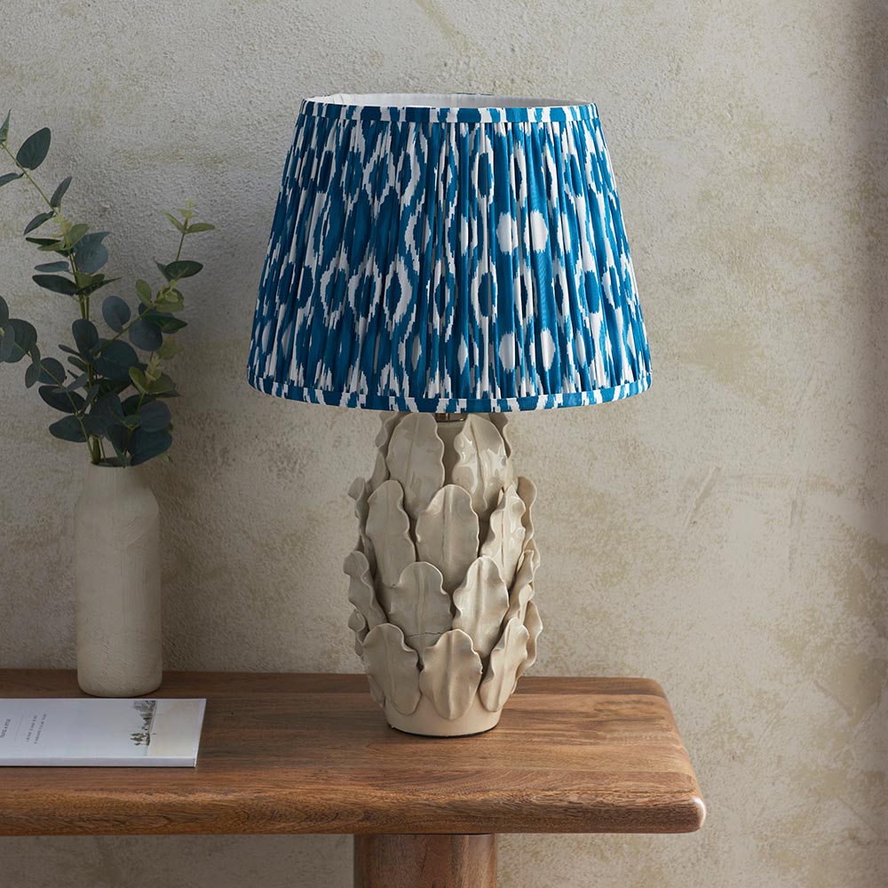 Endon Caldford Ikat 35cm table lamp with sculpted ivory ceramic leaf base and pleated blue Ikat shade on a wooden console beside a eucalyptus vase.