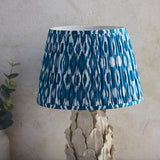 Endon Caldford Ikat 35cm table lamp with a pleated blue and cream Ikat shade on an ivory ceramic leaf-sculpted base against a pale wall.