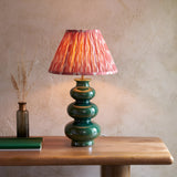 Carlstead Ikat Table Lamp in dark green glossy ceramic with pleated pink and orange patterned shade, shown on a wooden console table.