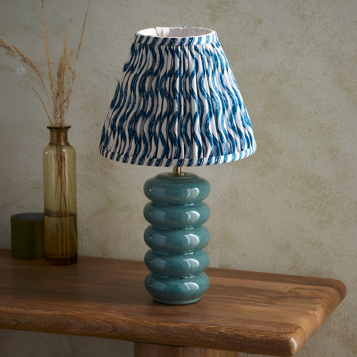 Cliffstead Table Lamp with stacked teal ceramic base and blue and white patterned tapered fabric shade, styled on a wooden table beside a glass vase.