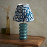 Cliffstead Table Lamp with stacked teal ceramic base and blue and white patterned tapered fabric shade, styled on a wooden table beside a glass vase.