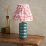 Cliffstead Table Lamp with ribbed teal ceramic base and pleated pink wave-print fabric shade, styled on a wooden table beside dried grasses.
