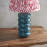 Cliffstead table lamp with ribbed teal ceramic base and pink striped tapered fabric shade, shown on a wooden surface against a plain wall.