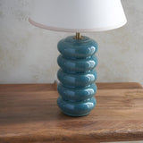 Endon Cliffstead ceramic table lamp with stacked ocean spray blue-green glazed base, antique brass stem and white Ivy shade on a wooden surface.