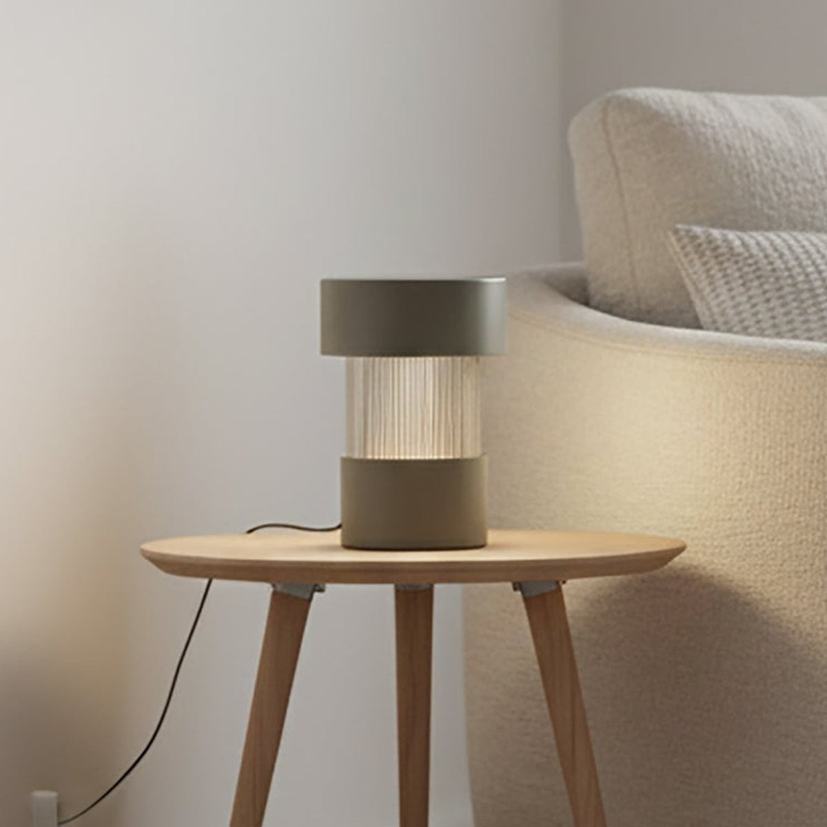 Balise Cylinder Ribbed Glass Lantern Table Lamp in green, with fluted glass midsection and iron top and base, shown lit on a side table beside a sofa.