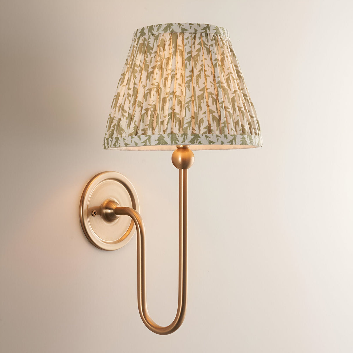 Cliffleigh Leaf Wall Light with a brushed brass wall mount and arm, topped by a pleated green leaf-print fabric shade, shown against a plain light background.