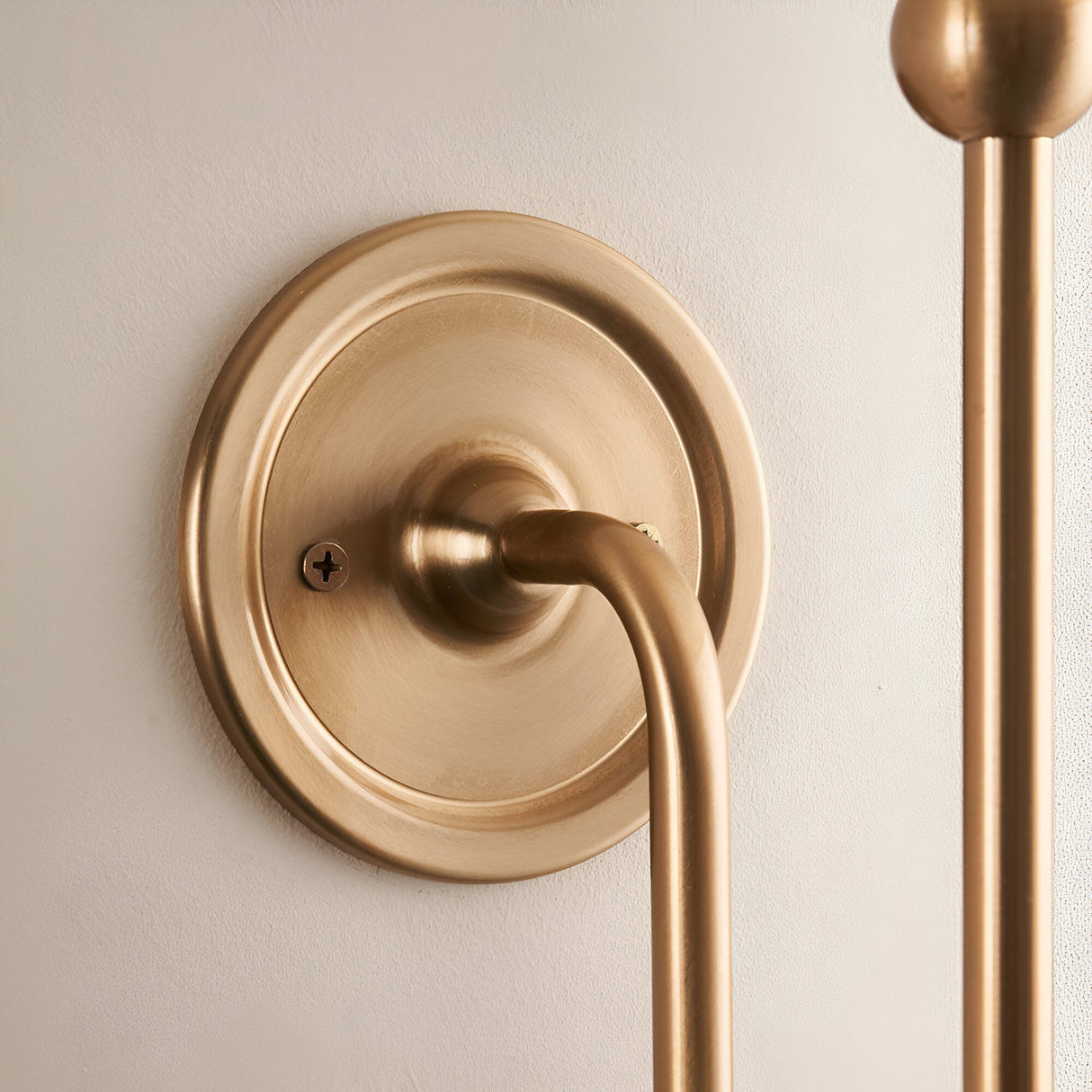 Close-up of the Cliffleigh Leaf Wall Light's brushed brass wall backplate and curved arm with visible fixing screw, shown without the fabric shade.