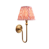 Endon Cliffleigh wall light with a slim brushed aged brass arm and tapered hand-pleated coral pink Ripple faux linen shade, on a white background.
