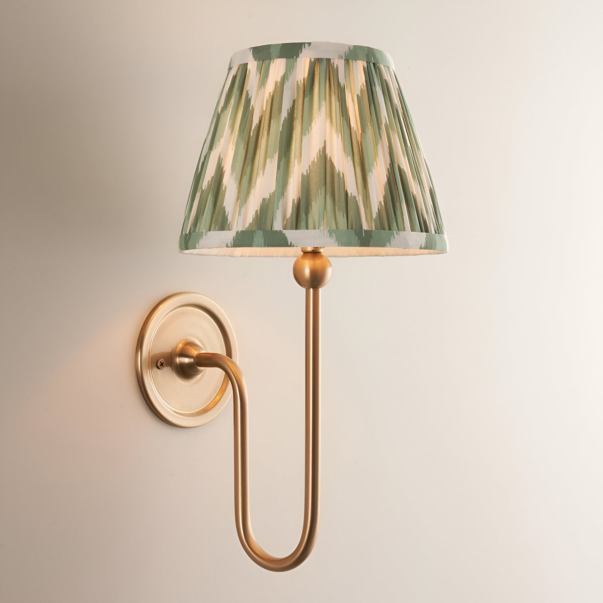 Endon Cliffleigh wall light with brushed aged brass curved arm and tapered pleated faux silk shade in green Zigzag pattern, on a neutral background.