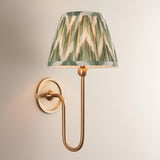 Endon Cliffleigh wall light with brushed aged brass curved arm and tapered pleated faux silk shade in green Zigzag pattern, on a neutral background.