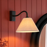 Endon Brockwood wall light with curved matt black arm and tapered natural linen shade, mounted on a red panelled wall beside a round black-framed mirror.