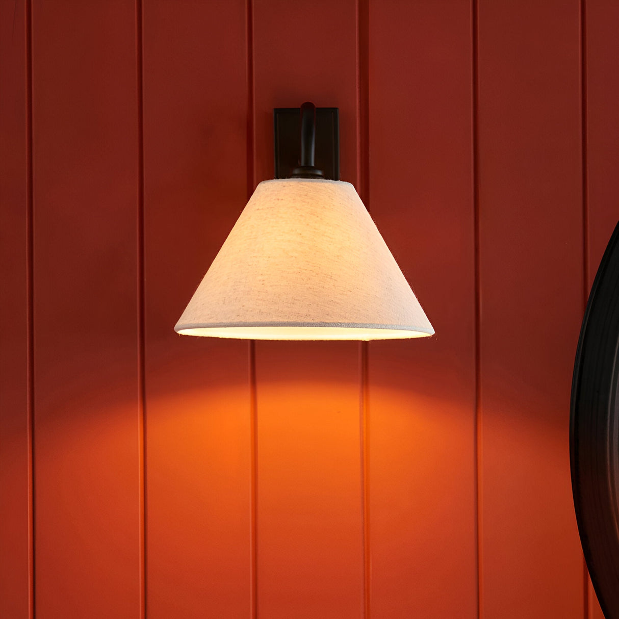 Endon Brockwood wall light with slim matt black arm and tapered natural linen shade, illuminated against a deep red panelled wall.