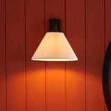 Endon Brockwood wall light with slim matt black arm and tapered natural linen shade, illuminated against a deep red panelled wall.