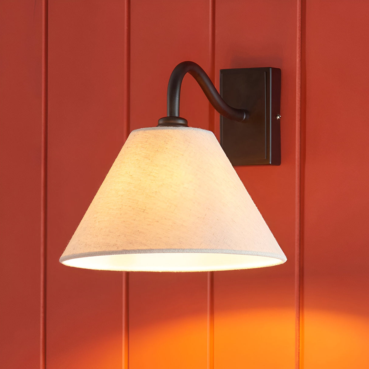 Endon Brockwood wall light with curved black metal arm and tapered natural linen shade, mounted on a red panelled wall.