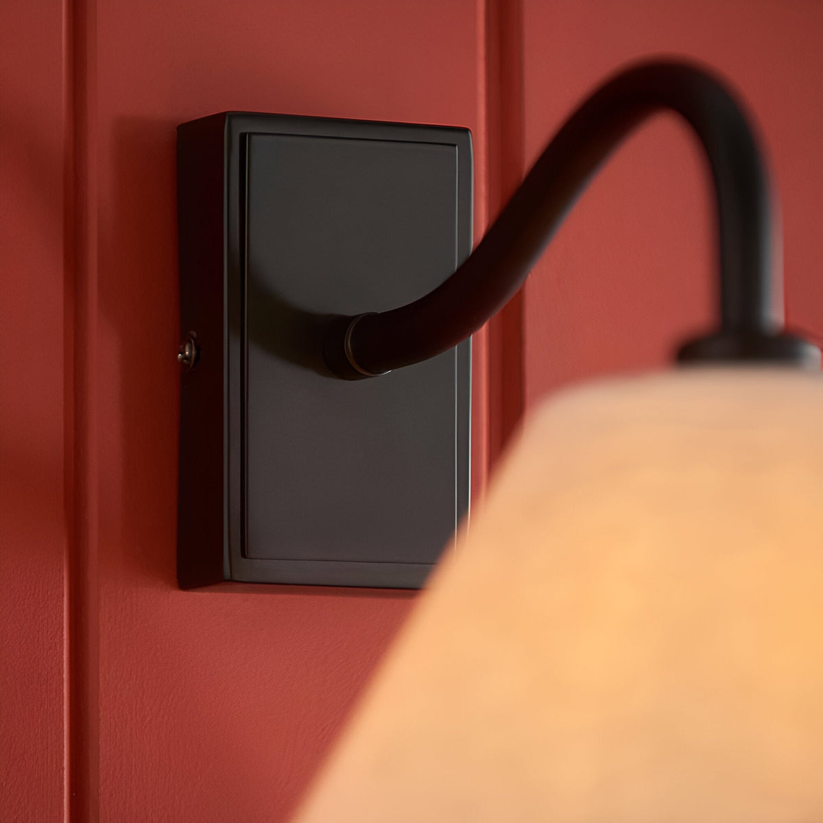 Endon Brockwood wall light close-up with matt black rectangular backplate and curved arm on a deep red panelled wall, linen shade softly lit.