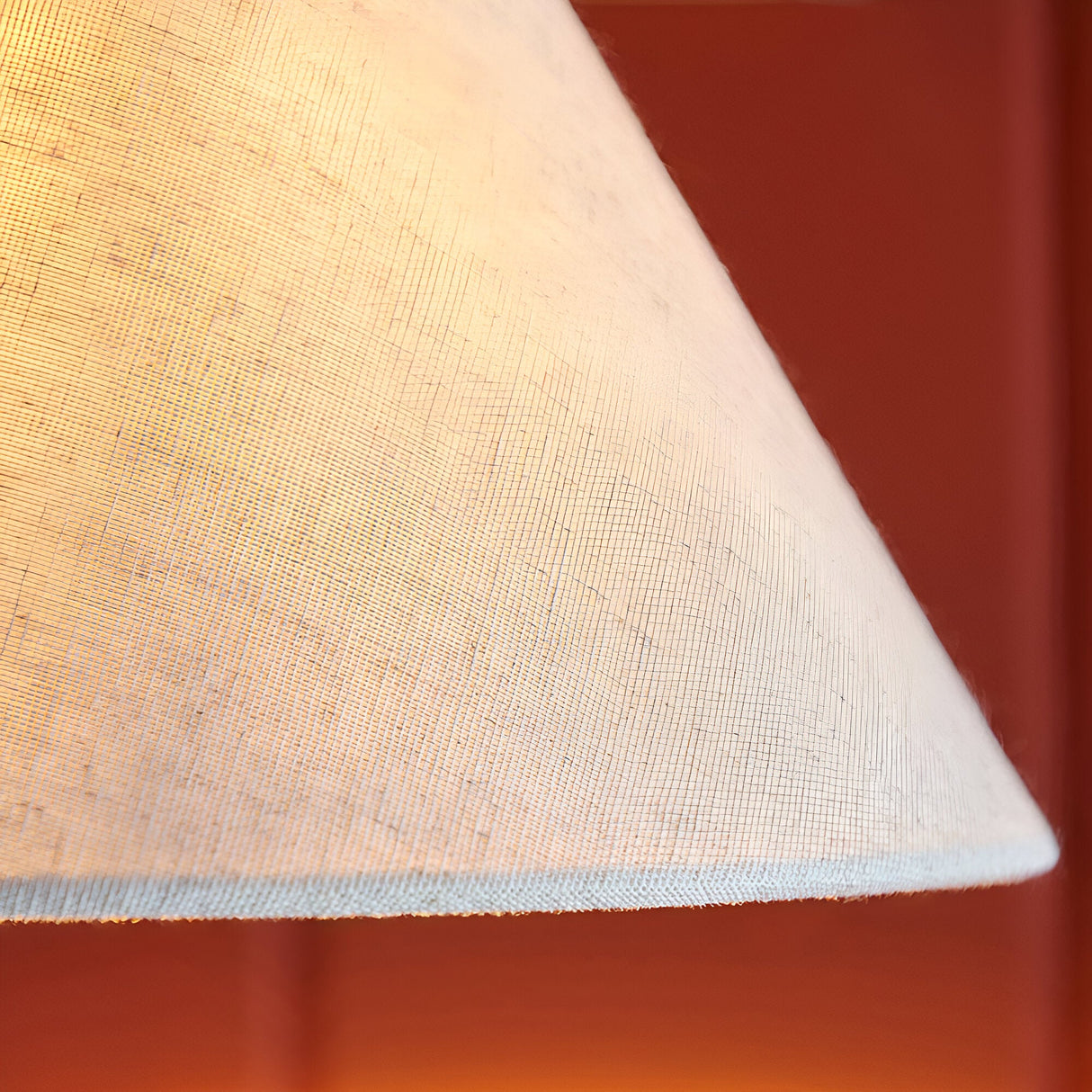 Close-up of the Endon Brockwood wall light's tapered natural faux linen shade, illuminated warmly against a deep terracotta wall.