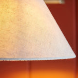Close-up of the Brockwood Wall Light's tapered natural linen shade, showing textured fabric and stitched edge against a warm brass glow.