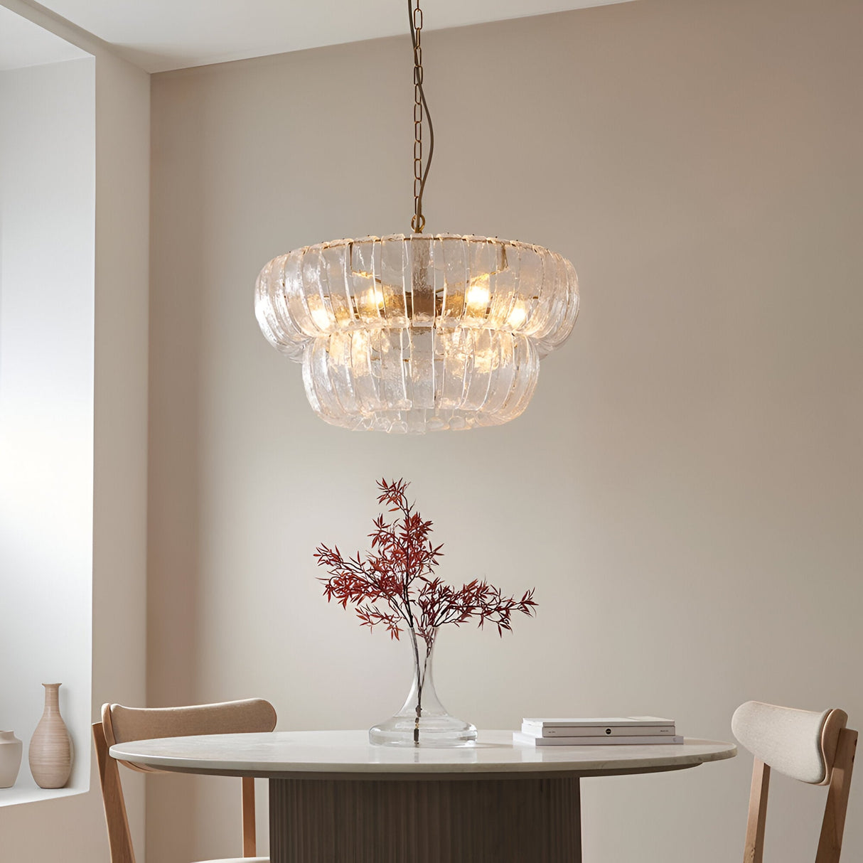 Carlwell 6 Light Pendant in brass, tiered curved clear glass design hanging above a dining table with a vase of red foliage in a neutral room.