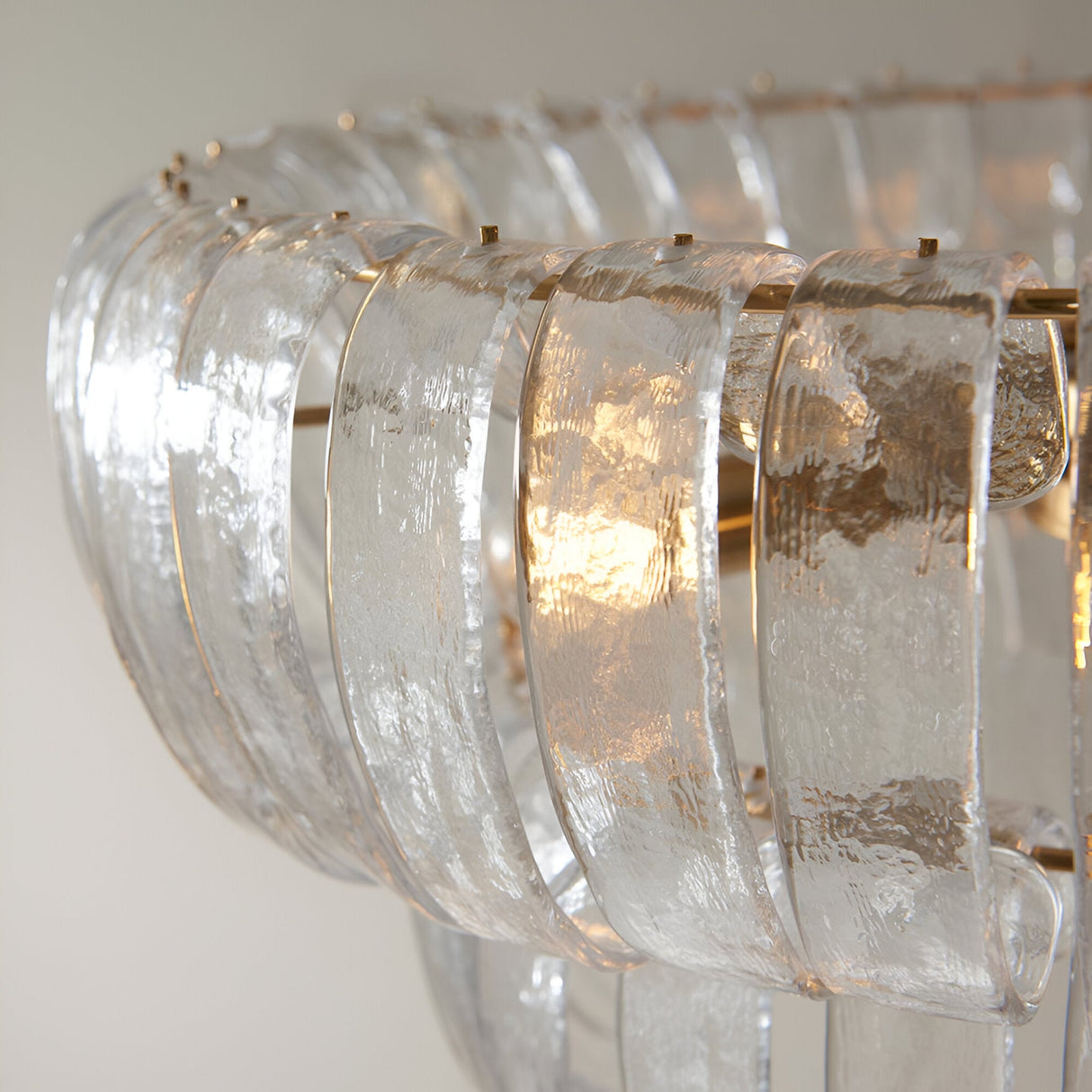 Close-up of the Carlwell 6 Light Pendant, showing curved textured glass panels tiered around a brushed antique brass frame.